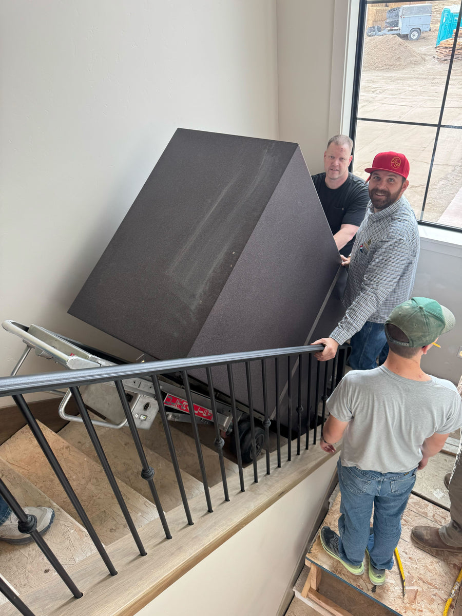 Large safe being guided up a stair landing by a delivery team inside a home under construction.